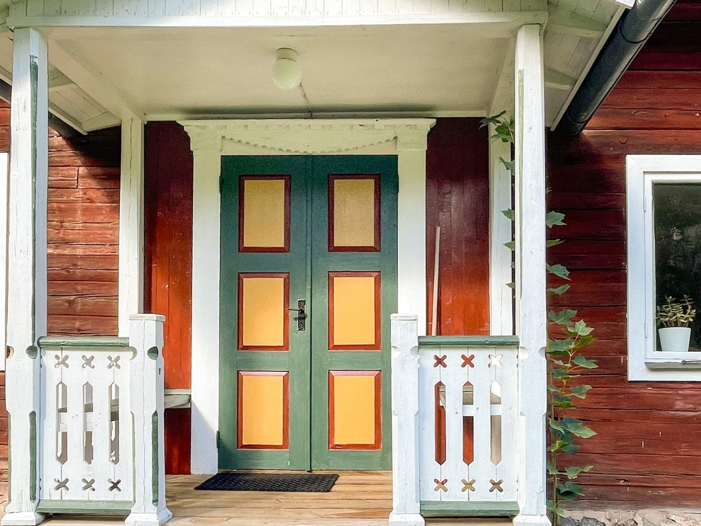 Une maison en bois avec une porte verte, des colonnes blanches sur le porche et une petite fenêtre.