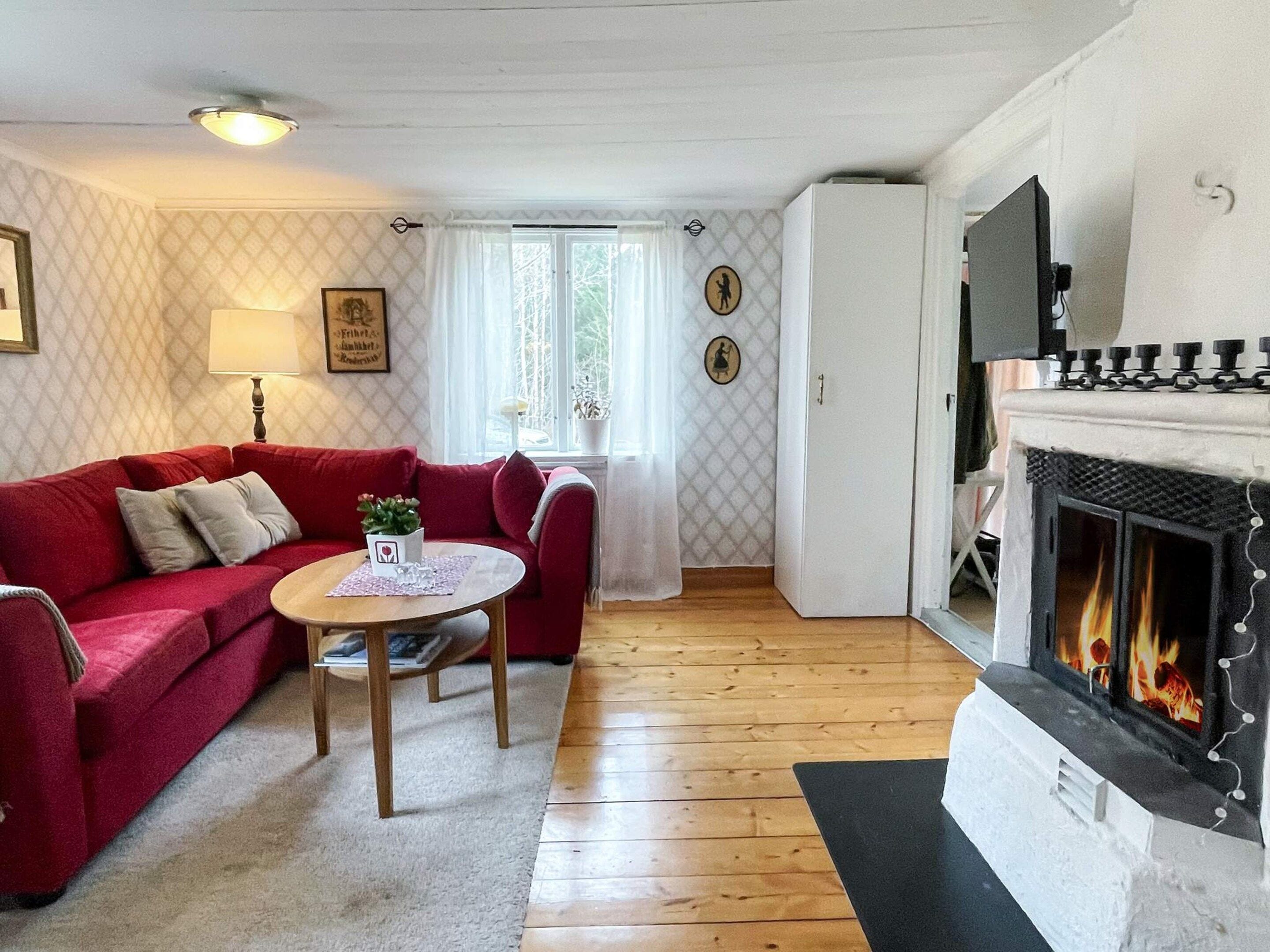 Una sala de estar acogedora con un sofá rojo, una mesita con una planta, una chimenea y un papel tapiz estampado.