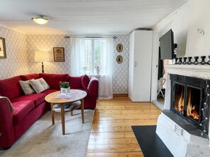 Una sala de estar acogedora con un sofá rojo, una mesita con una planta, una chimenea y un papel tapiz estampado.