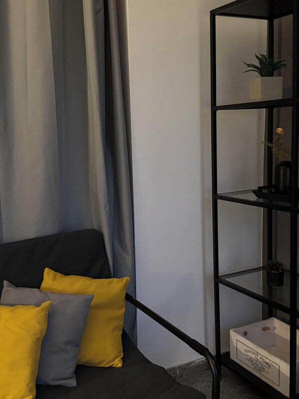 Ein Zimmer mit einem schwarzen Sofa, gelben und grauen Kissen, einem schwarzen Metallregal mit Pflanzen und einer weißen Box mit der Aufschrift 'VINTAGE HOME'.