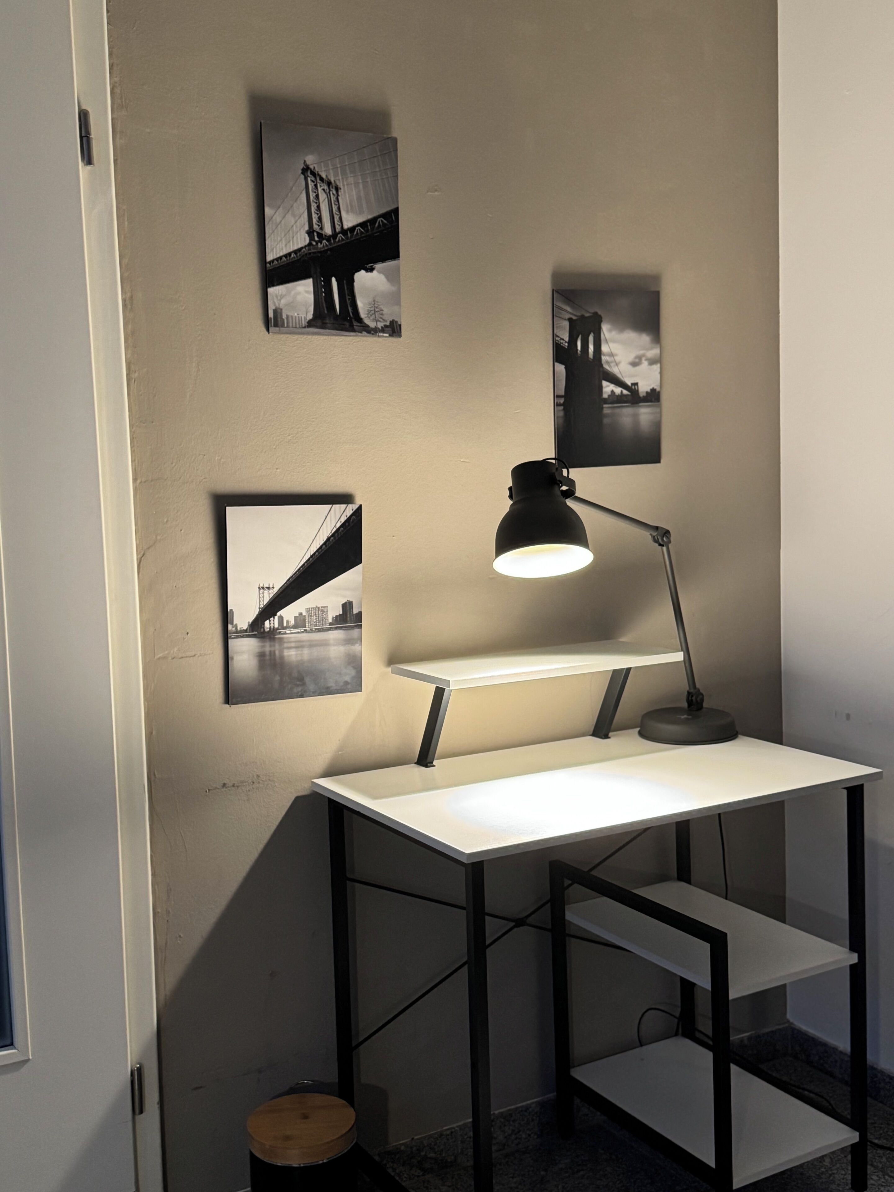 Ein Schreibtisch mit einer Lampe und drei schwarz-weißen Fotografien an der Wand.