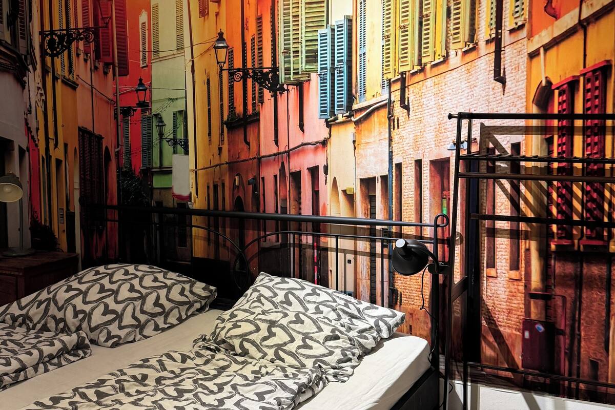 Una cama con almohadones estampados en una habitación con un mural de edificios coloridos.