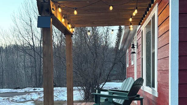 Une terrasse en bois avec un espace salon couvert, une guirlande de lumières et un bâtiment rouge en arrière-plan.