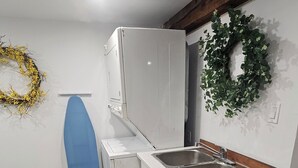 Ett kompakt kök med en inbyggd diskho, en blå strykjärnsbräda och en dekorativ krans på väggen.
