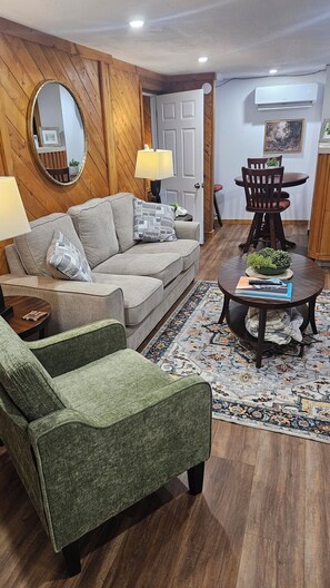 Una sala de estar con sofá, sillón, mesa de centro y un comedor con una silla y mesa.