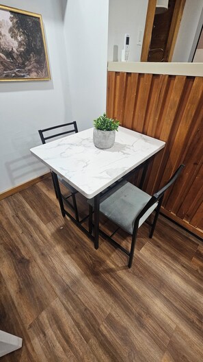 Een eettafel met een marmeren blad, omringd door vier stoelen, een potplant en een houten scheidingswand.
