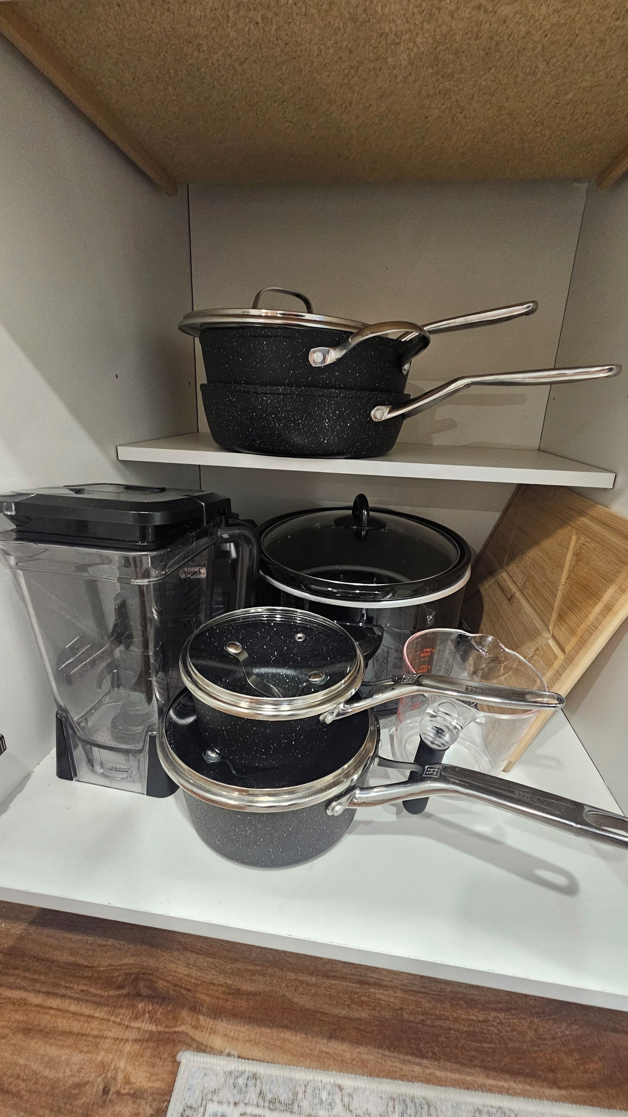 Uma cozinha com bancada branca, tábua de corte de madeira e diversos utensílios, incluindo panelas e frigideiras.