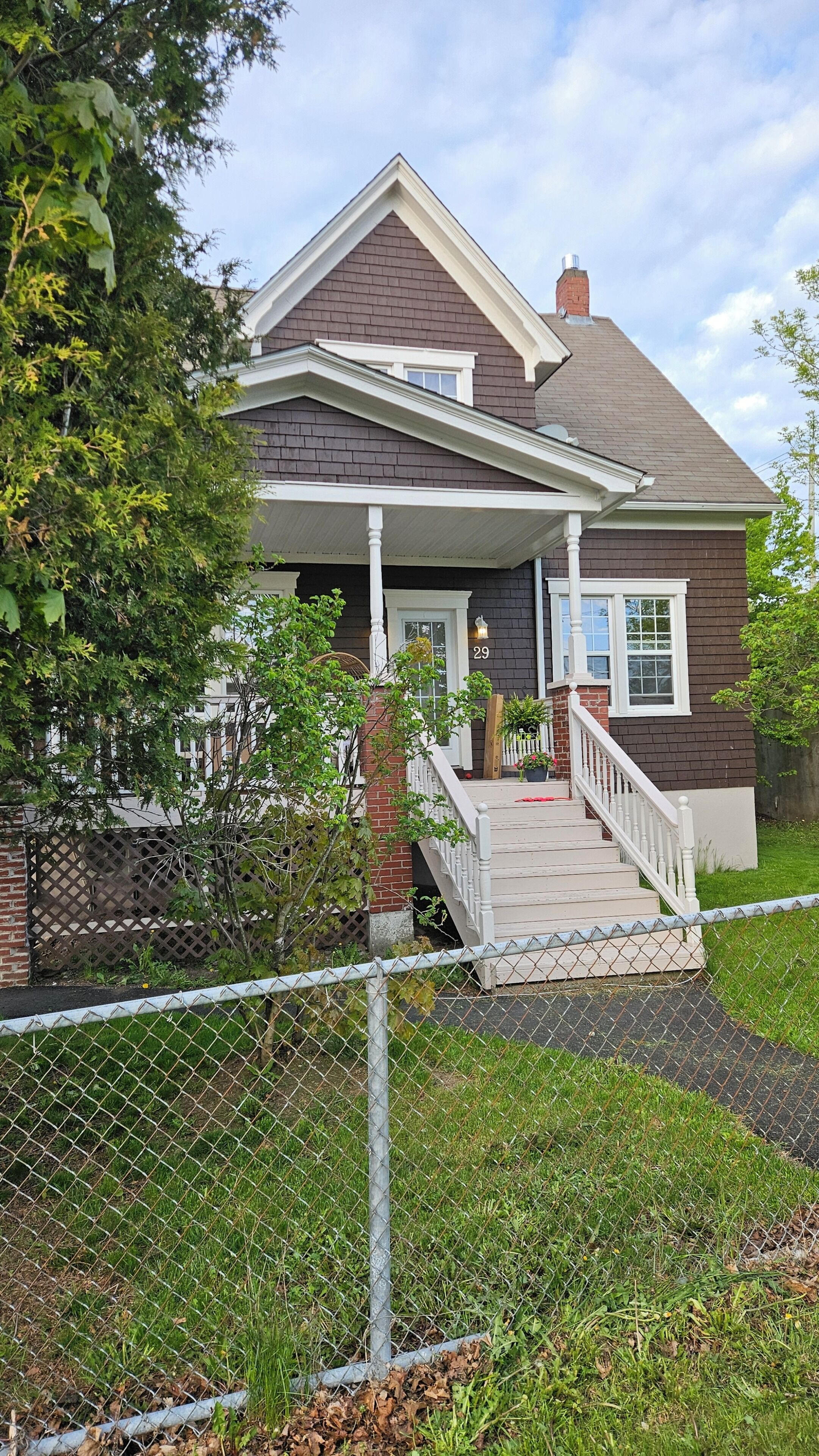 Une maison à deux étages avec un porche à l’avant, une cheminée en briques et le numéro « 29 » affiché sur la façade.