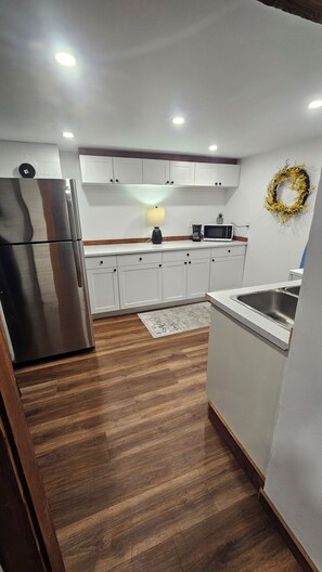 A kitchen with white cabinets, a stainless steel refrigerator, a microwave, and a sink.