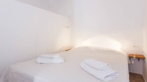 Un dormitorio con cama, dos toallas enrolladas, una mesita de noche y una lámpara de pared.