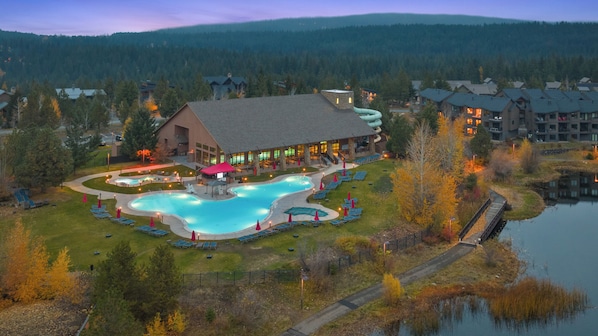 A resort with a large swimming pool, a covered area, and a view of a forested mountain range. - Luxury 2BR Penthouse with Lodge Pool Access in Suncadia Resort (Cle Elum)