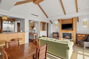 A modern living room with a fireplace, a dining area with wooden furniture, and a kitchen with stainless steel appliances. - Luxury 2BR Penthouse with Lodge Pool Access in Suncadia Resort (Cle Elum)