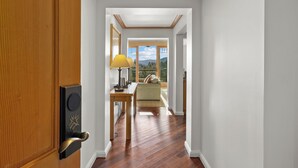 Un couloir avec une porte en bois, une table avec une lampe, un canapé et une fenêtre donnant sur l’extérieur.