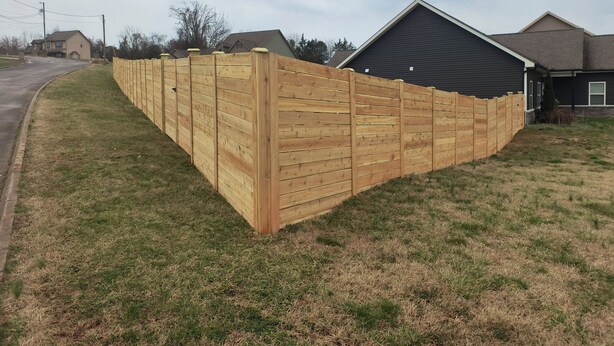 A wooden fence along a grassy area with a house in the background.