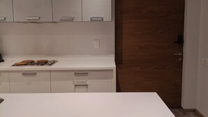 A modern kitchen with white cabinets, a white countertop, and a wooden door. - Modern apartment with pool and gym in TOP location in the CDMX (Ciudad de México)