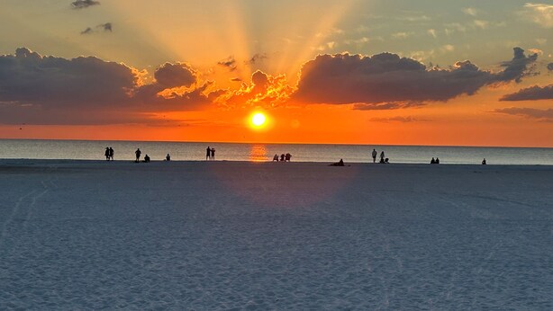 A beach scene with a sunset, calm sea, and silhouettes of people. - Great beach access, central location, 2-bedroom condo in wonderful Marco Island (Marco Island)