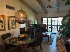 Ein Wohnzimmer mit Glastisch, Stühlen, einer Couch, einem Fernseher und einem Deckenventilator.