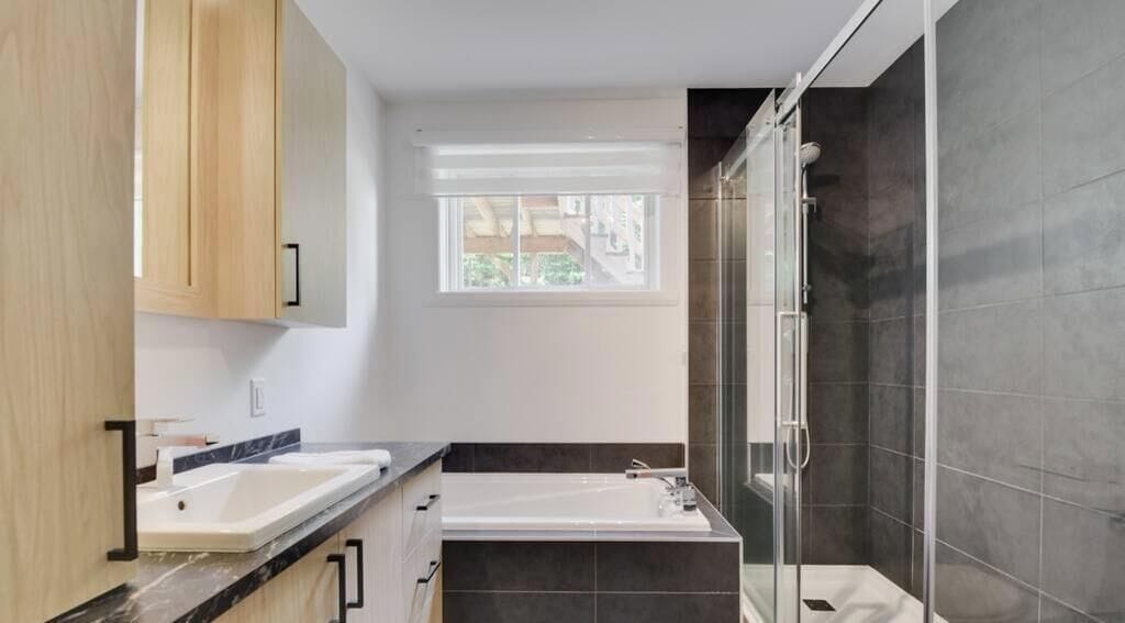Een moderne badkamer met een bad, twee wastafels, een raam en een douchegedeelte.