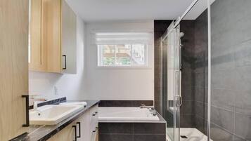 Een moderne badkamer met een bad, twee wastafels, een raam en een douchegedeelte.