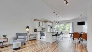 A modern kitchen with a central island, bar stools, and pendant lighting. - Atlas | Familial | Piscine & Spa by Alchalet (Pont-Rouge)