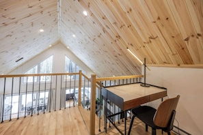 Une chambre à coucher aménagée en mezzanine, avec un plafond en pente, un bureau avec une chaise et une vue sur l’extérieur.