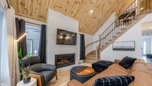 Una sala de estar moderna con chimenea, sofás de cuero, televisor y una escalera.