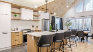 Una cocina moderna con una isla central, armarios de madera, un refrigerador de acero inoxidable y una zona de comedor con taburetes de bar.
