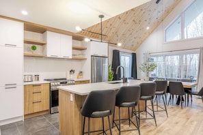 Une cuisine moderne dotée d’un îlot central, de meubles en bois, d’un réfrigérateur en acier inoxydable et d’un coin repas avec des tabourets de bar.