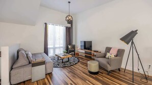 Un salón moderno con sofá, sillón, mesa de centro, televisor y lámpara de pie.