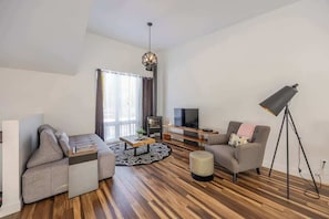 Uma sala de estar moderna com sofá, poltrona, mesa de centro, televisão e abajur.