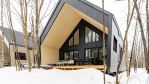 A modern house with a sloped roof, large windows, and a wooden deck. - ØM de Portneuf - Spa privé - Nature by Alchalet (Pont-Rouge)
