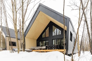 Ein modernes Haus mit Satteldach, großen Fenstern und einer Holzterrasse.