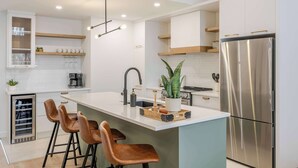 A modern kitchen with a central island, stainless steel appliances, and bar stools. - ØM de Portneuf - Spa privé - Nature by Alchalet (Pont-Rouge)