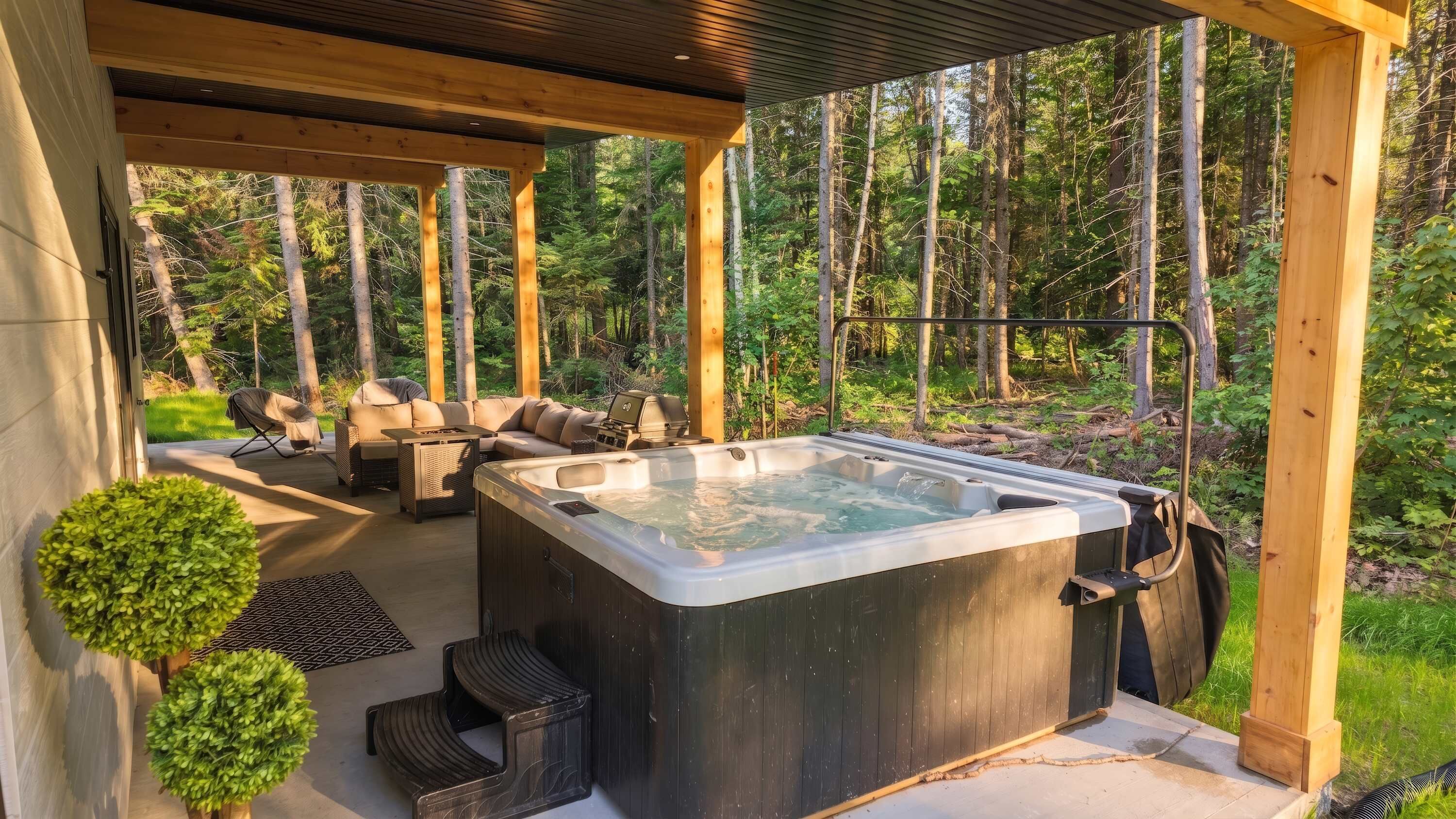 A hot tub under a wooden pergola with a forest backdrop.