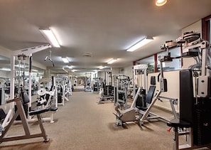 Ein Fitnessstudio mit verschiedenen Trainingsgeräten, Spiegeln und einem Teppichboden.