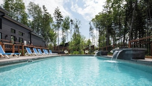 A swimming pool with lounge chairs, a waterfall feature, and a building with a dark facade.