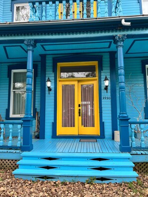 A blue house with a yellow door, a number '3930' on the door, and a porch with blue railings.