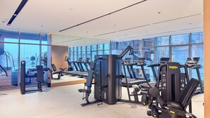 A gym with exercise equipment, large windows, and a clean, modern design. - PVH - Royal Regency - Modern Studio (Dubai)