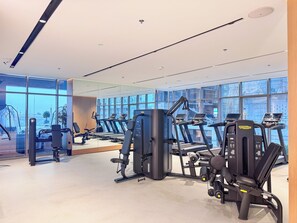 A gym with exercise equipment, large windows, and a clean, modern design. - PVH - Royal Regency - Modern Studio (Dubai)