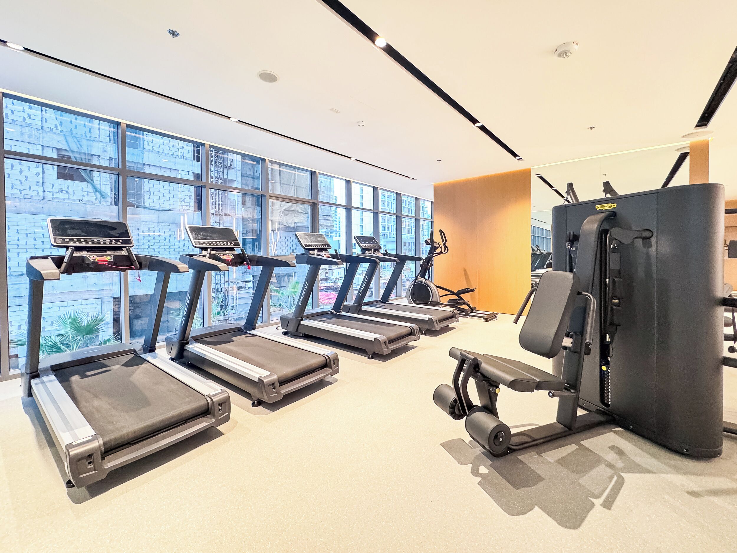 Ein Fitnessstudio mit Laufbändern, Kraftgeräten und großen Fenstern mit Blick auf die Stadt.