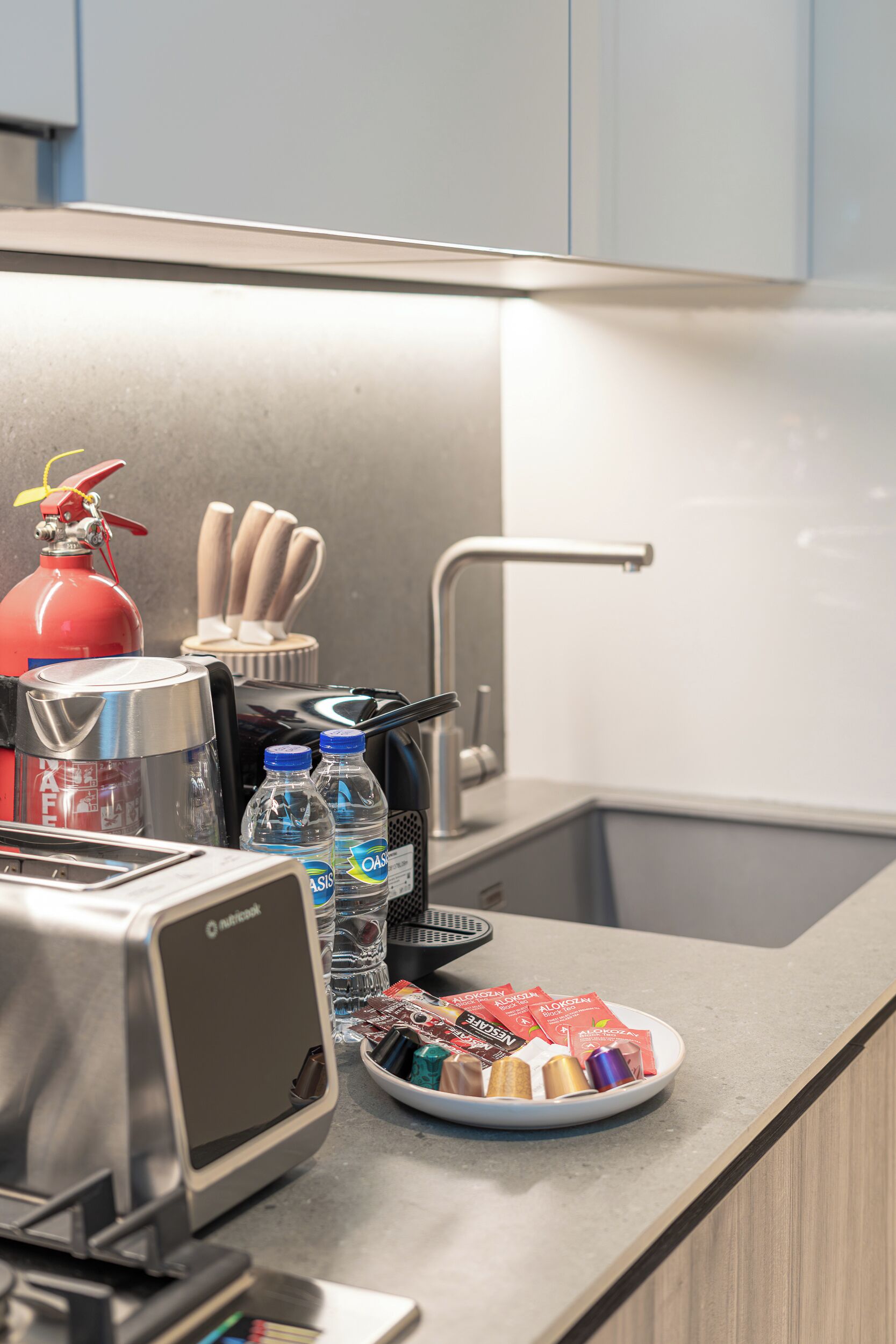A kitchen counter with a toaster, a red fire extinguisher, a sink, and a plate with snacks.