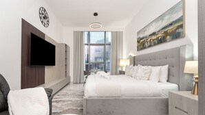A modern hotel room with a large bed, a flat-screen TV, a painting, and a city view. - PVH - Royal Regency - Modern Studio (Dubai)