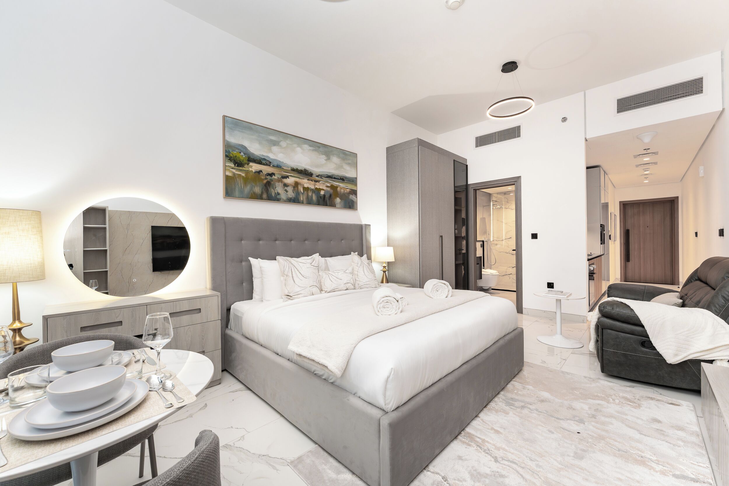 A modern bedroom with a large bed, a dining area with a table and chairs, a sofa, and a painting on the wall.