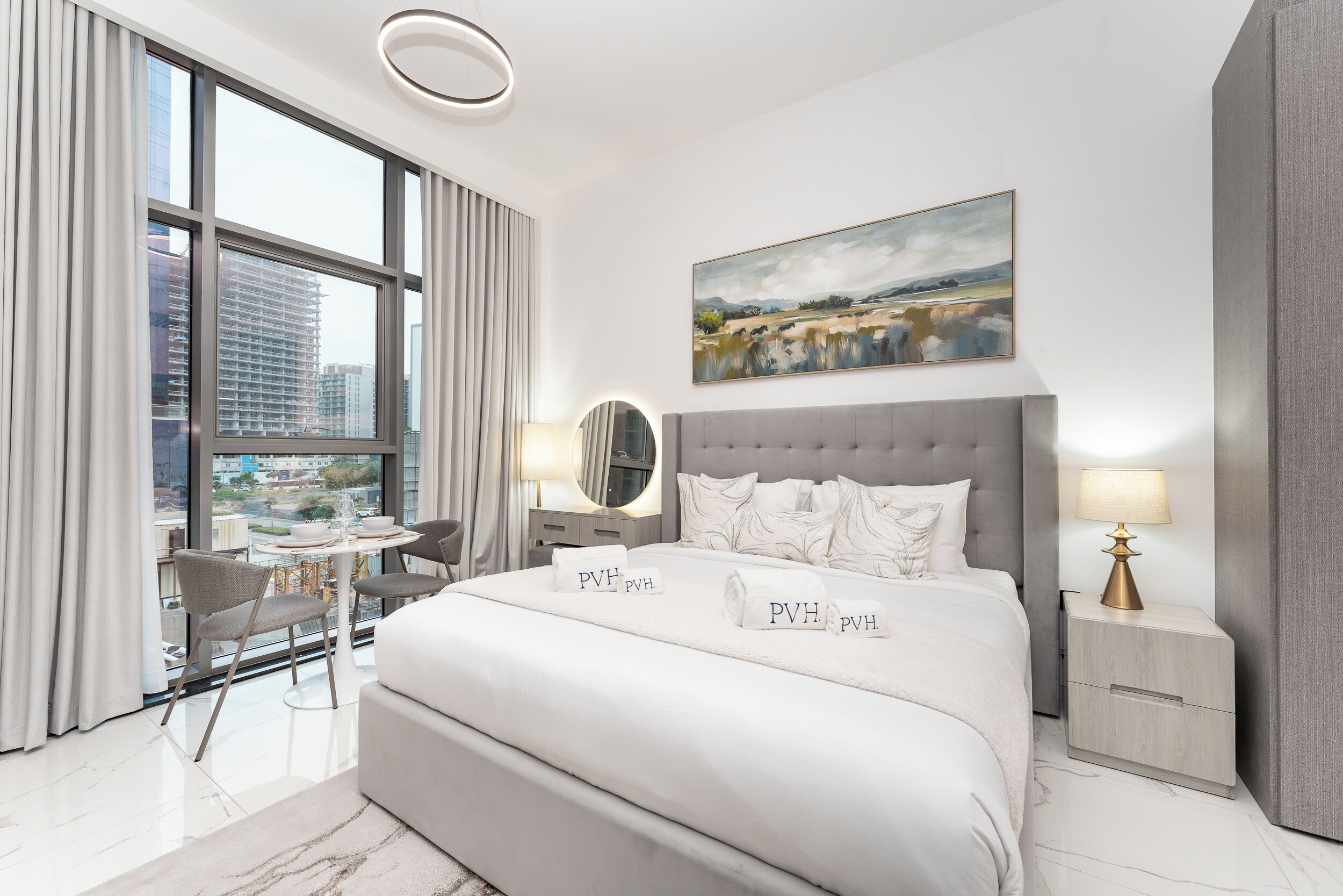 A modern hotel room with a large bed, bedside tables, a desk, and a view of the city.