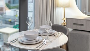 A dining table set with plates, bowls, glasses, and cutlery, with a lamp and curtains in the background. - PVH - Royal Regency - Modern Studio (Dubai)