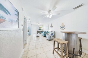 A spacious living area with a ceiling fan, a bar area with a stool, and a sofa with patterned cushions.