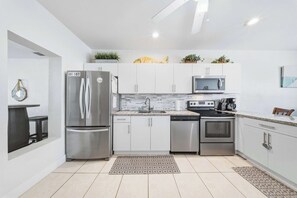 A modern kitchen with stainless steel appliances, white cabinetry, and a tiled floor.