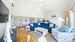 A living room with a blue sofa, a white coffee table, a patterned armchair, a small sailboat model, and a staircase leading to an upper level. - Sea Dreams on 9, 3 bedroom 3 bath 1/2 duplex, Private Pool in Key Colony Beach waterfront with 37 ft dockage and cabana club private membership, pool table and putting green. (Key Colony Beach)