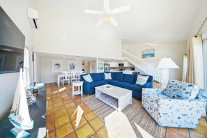 A living room with a blue sofa, a white coffee table, a patterned armchair, a small sailboat model, and a staircase leading to an upper level. - Sea Dreams on 9, 3 bedroom 3 bath 1/2 duplex, Private Pool in Key Colony Beach waterfront with 37 ft dockage and cabana club private membership, pool table and putting green. (Key Colony Beach)