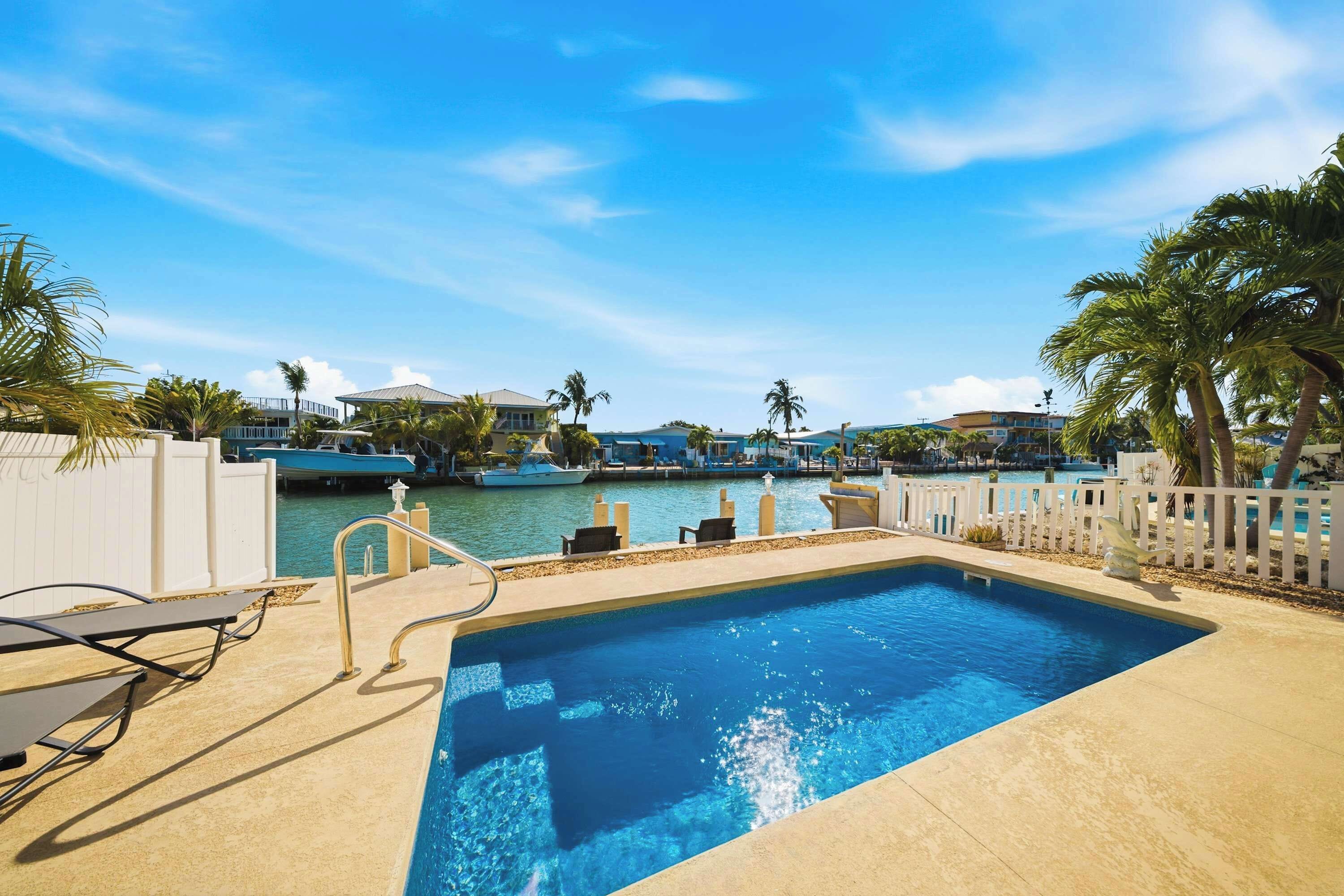 A swimming pool with lounge chairs and a view of boats and buildings.